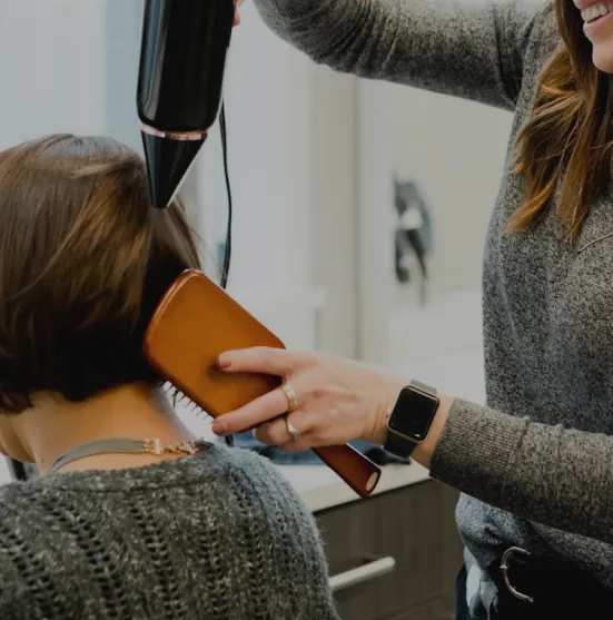 Peluquera secando el pelo a una clienta con secador y cepillo